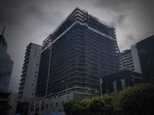 Load image into Gallery viewer, International Apartments under construction, covered in scaffolding and scrim

